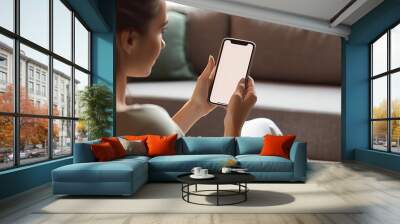 Young woman using smart phone at home, white blank empty screen. Girl texting on mobile phone indoor. Connection, technology, apps, smartphone mock up, communication concept Wall mural