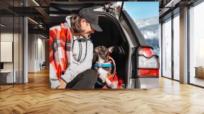 Man and french bulldog dog sitting on car trunk against winter landscape Wall mural