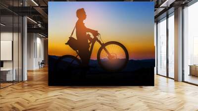 Silhouette young man and bike on muontain, sunset. Wall mural