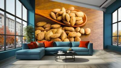 Almonds seeds pour from wood spoon on textured wooden background, top view. Wall mural