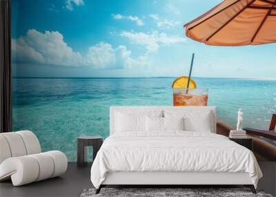 A hand is seen holding a cocktail, resting on a beach chair under a large sun umbrella, with a tranquil ocean in the background Wall mural