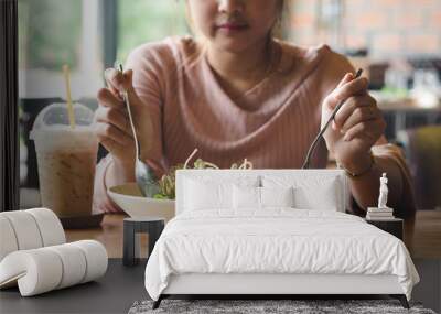 Asian woman holding fork and spoon to eating vegetable salad with a cup of coffee at lunch in cafe. Wall mural