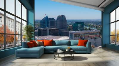 Aerial perspective of Sacramento, California, highlighting the Golden 1 Center, high rise buildings, and the Sacramento River under a clear blue sky. Wall mural