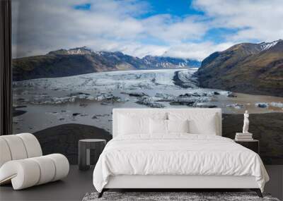 Stunning aerial view of a light blue glacial lake with white ice, surrounded by brown and green mountains, showcasing the beauty of Iceland's landscape. Wall mural