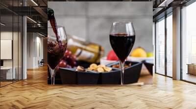 Red wine pouring into a wine glass at a tasting with various types of appetizers.  Wall mural