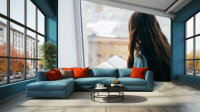 Young girl reading with book by the window Wall mural