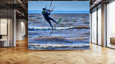 A male kiteboarder jumps above the surface of the water of a large river.  Splashes of water scatter in different directions.  Wall mural