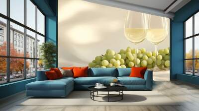 A pair of wine glasses filled with white wine, placed on the table next to grapes, bathed in soft light  Wall mural