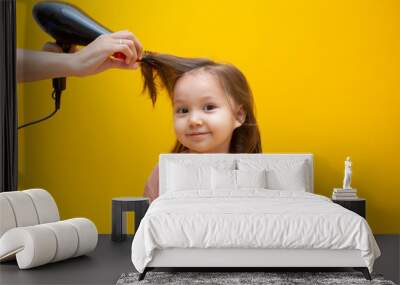 The hairdresser dries the hair of a little girl with a comb. Wall mural