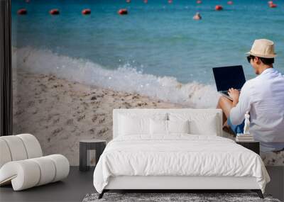 Banner Man traveler use laptop on summer beach blue sky. Asian man travel relax sitting summer beach island. Man typing laptop computer holiday business trip freelance working online with copy space Wall mural