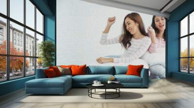 Two young women dance laughing together happy friendship smile with happiness in bedroom wear casual dress on bed. Happy girl friends dance to celebrate good news together at home. Woman joyful laugh Wall mural