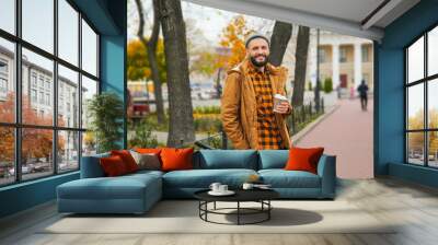 Attractive young hipster with cup of coffee and bicycle on city street Wall mural