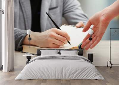 Author signing autograph in own book at wooden table Wall mural