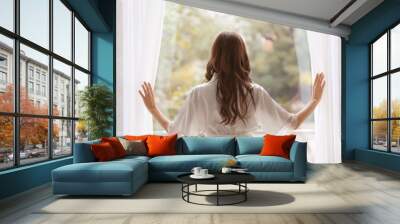 Beautiful woman in white silk robe standing near window Wall mural