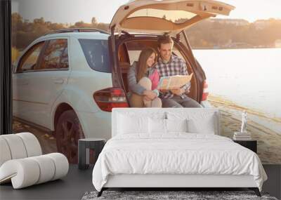 Beautiful young couple with map sitting in car trunk near river Wall mural