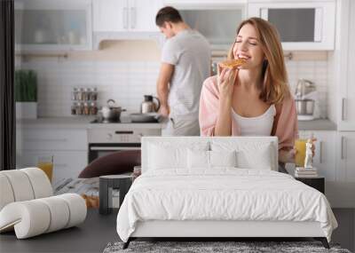 Beautiful young woman having breakfast while her beloved boyfriend cooking in kitchen Wall mural