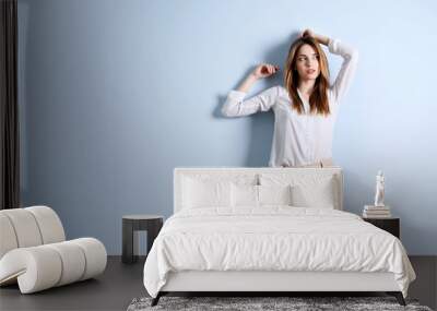 Beautiful young woman in a white shirt and beige pants on blue wall background Wall mural