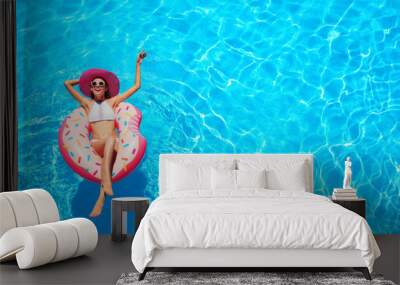 Beautiful young woman relaxing on inflatable donut in blue swimming pool Wall mural