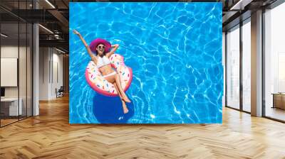 Beautiful young woman with inflatable donut in blue swimming pool Wall mural