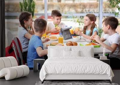 Children sitting at cafeteria table while eating lunch Wall mural