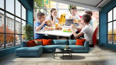 Children sitting at cafeteria table while eating lunch Wall mural