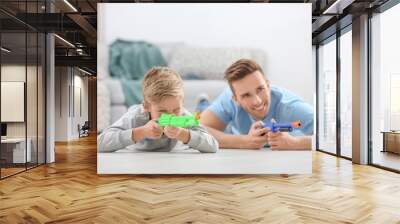 Cute boy and his father playing with toy guns at home Wall mural