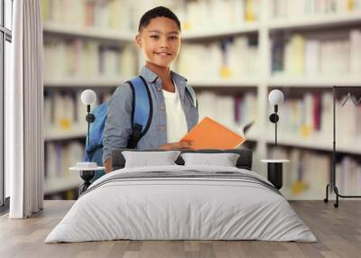 cute boy with backpack holding book on blurred book shelves background. library concept. Wall mural