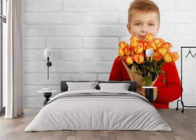 Cute boy with bouquet of beautiful flowers near light brick wall Wall mural