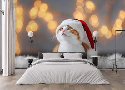 Cute cat in Santa Claus hat against blurred Christmas lights Wall mural