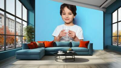 Cute little boy drinking water from glass on blue background Wall mural