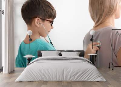 Cute little boy in doctor uniform examining patient indoors Wall mural