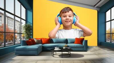 Cute little boy in headphones listening to music on color background Wall mural