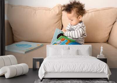 Cute little child with colorful book on sofa at home Wall mural