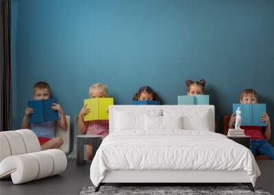 Cute little children reading books while sitting near color wall Wall mural