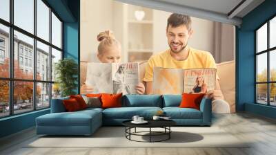 Cute little girl and her father reading magazines at home Wall mural