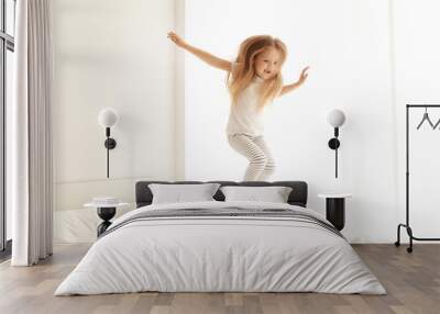 Cute little girl jumping on white bed Wall mural