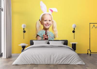 Cute little girl with bunny ears and chocolate rabbit on color background Wall mural