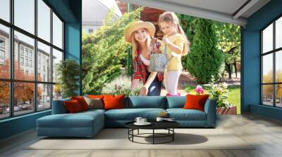 Cute little girl with mother taking care of plants in garden on sunny day Wall mural