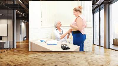 Elderly doctor measuring waist of overweight woman in hospital Wall mural