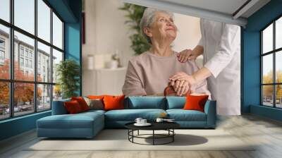 Elderly woman holding hands on walking stick and listening doctor in light room Wall mural