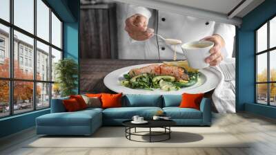 Female chef pouring sauce onto plate with delicious salmon in kitchen Wall mural