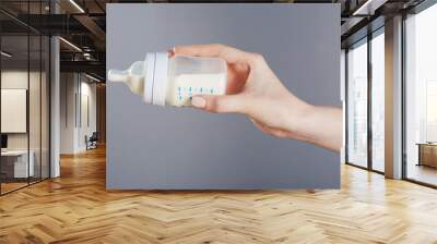 Female hand holding a baby bottle of milk on color background Wall mural