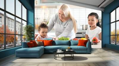 Female mature nanny feeding little African-American girl in kitchen Wall mural