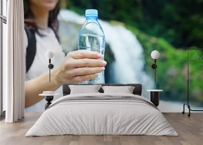 Female tourist holding bottle of clear water on blurred river background Wall mural