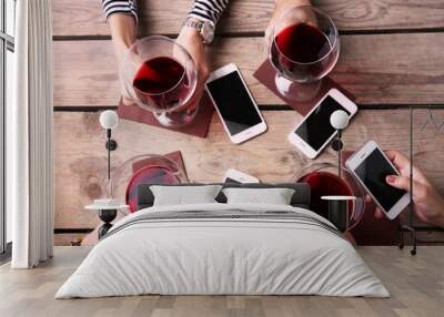 Four hands with smart phones holding glasses with red wine, on wooden table background Wall mural