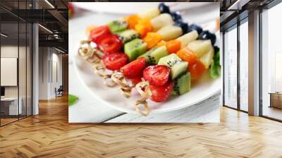 Fresh fruits on skewers in plate on wooden table, closeup Wall mural