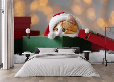 Gift box with cute cat in Santa Claus hat against blurred Christmas lights Wall mural