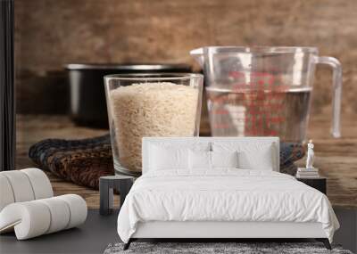 Glass of rice and measuring jug with water on wooden table Wall mural