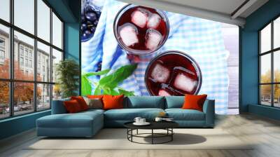 Glasses of fresh blackcurrant juice with ice cubes on checkered napkin on wooden table, top view Wall mural