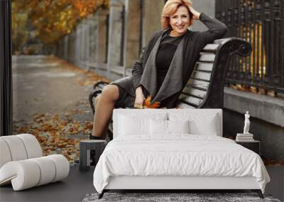 Gorgeous middle aged woman sitting on bench in autumn park Wall mural